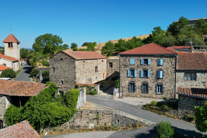 Vue sur le village de Saint-Privat du Dragon et ses maisons en pierre aux volets bleus, entourées de verdure.