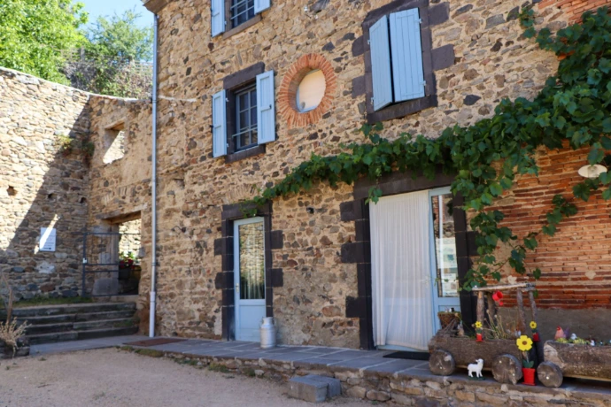 Façade en pierre de la Maison Chaumet avec ses volets bleus, ses plantes grimpantes et son entrée.